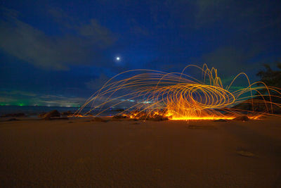 Light trails on beach against sky at night