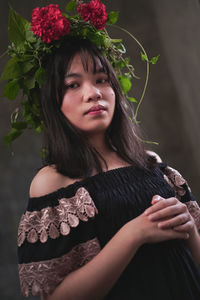 Portrait of beautiful young woman standing against red flowering plants