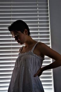 Young woman looking down while standing against window