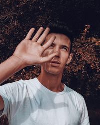 Young man looking away while gesturing against tree