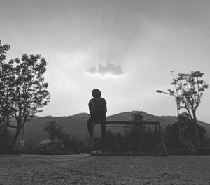 Rear view of silhouette woman sitting on railing against sky during sunset