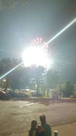 People by illuminated trees against sky at night
