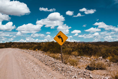 Road sign on landscape against sky