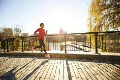 A backlit woman running over a footbridge in a city park.