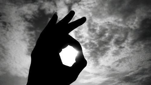Silhouette hand forming ok sign against sky