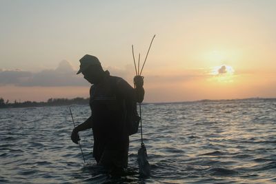 Silhouette man fishing on sea against sky during sunset