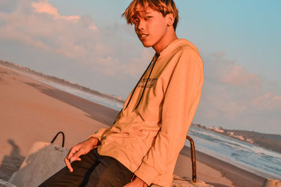 Woman sitting on shore at beach against sky during sunset