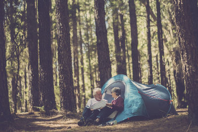 Couple reading map while sitting by tent against trees