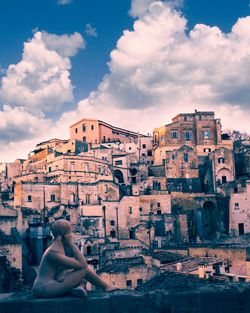 Woman sitting on buildings in city against sky at sunset