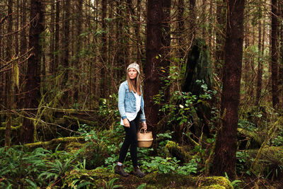 Young woman standing by tree trunk in forest