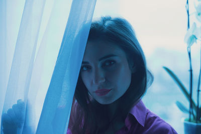 Portrait of young woman looking through window