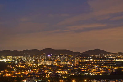 Illuminated city by sea against sky at night