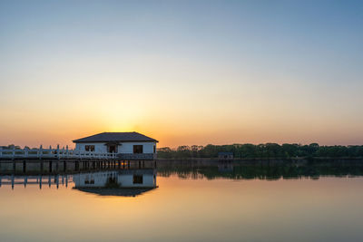 House by lake against sky during sunset