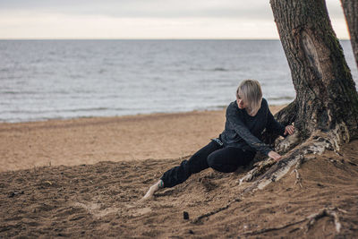 Man sitting on tree trunk at beach against sky