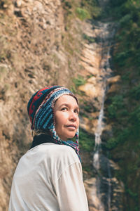 Woman in warm clothing against waterfall