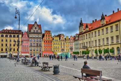 People walking in city against cloudy sky