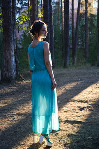 Woman standing by tree trunk in forest