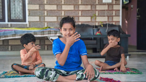 Three indian little kids doing meditate yoga asana on roll mat at home.