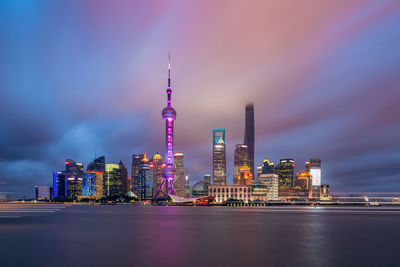 Illuminated buildings in city against cloudy sky