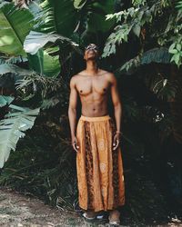 Full length of shirtless man standing against tree