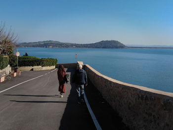 Rear view of people on road by sea against clear sky