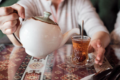 A hand holds a teapot and pours black tea into a turkish cup. tea drinking in an asian cafe