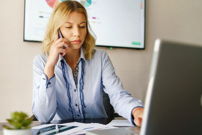 Young woman using mobile phone while sitting on table