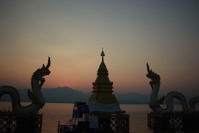 Statues at lake against sky during sunset