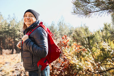 Smiling woman enjoying hike on sunny vacation day. female with backpack walking through forest