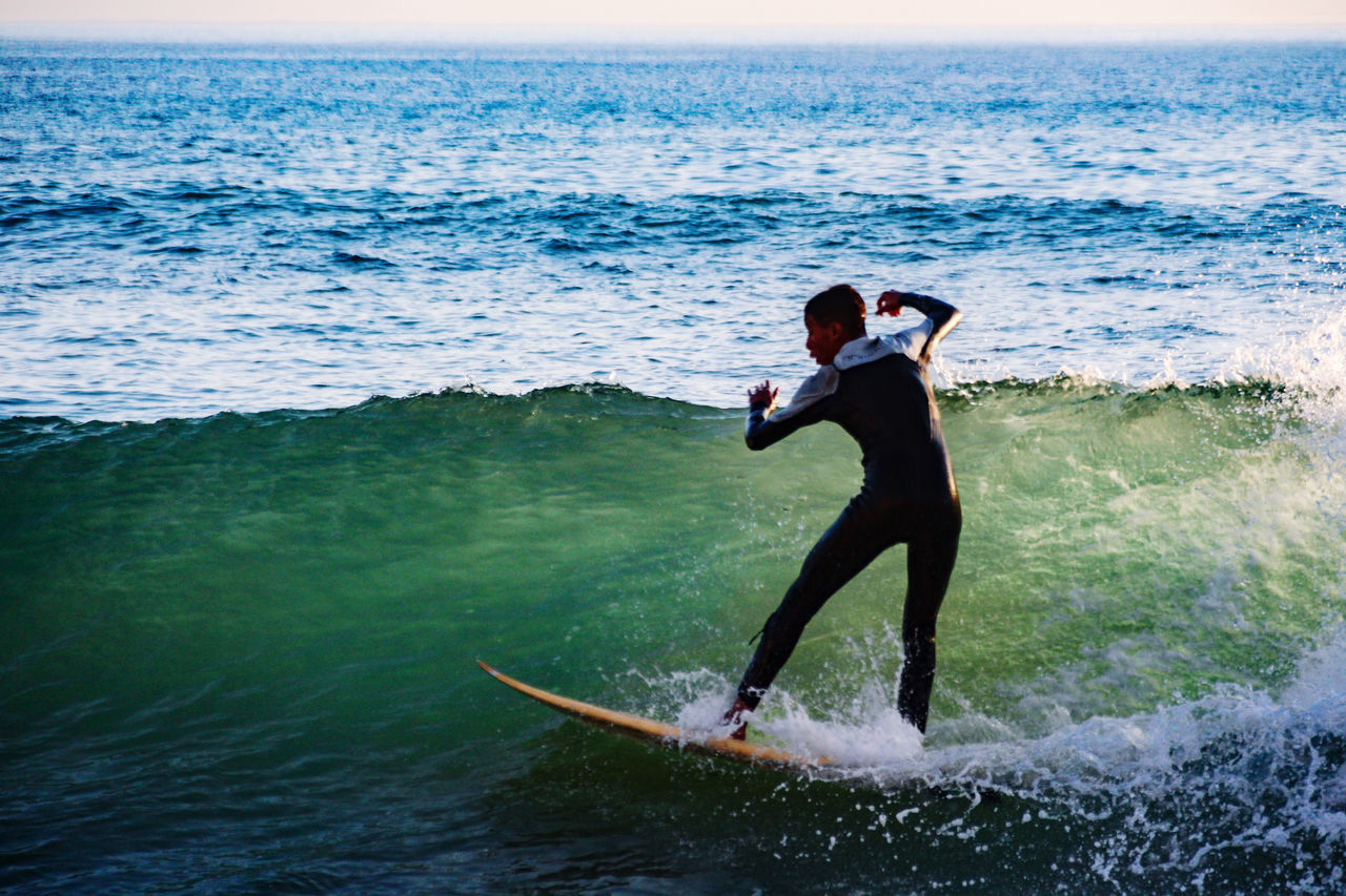 REAR VIEW OF MAN WITH SURFBOARD ON SEA