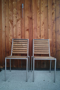 Empty chairs against wooden wall