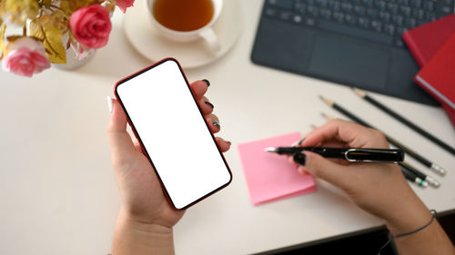 Cropped hands of woman using smart phone against white background