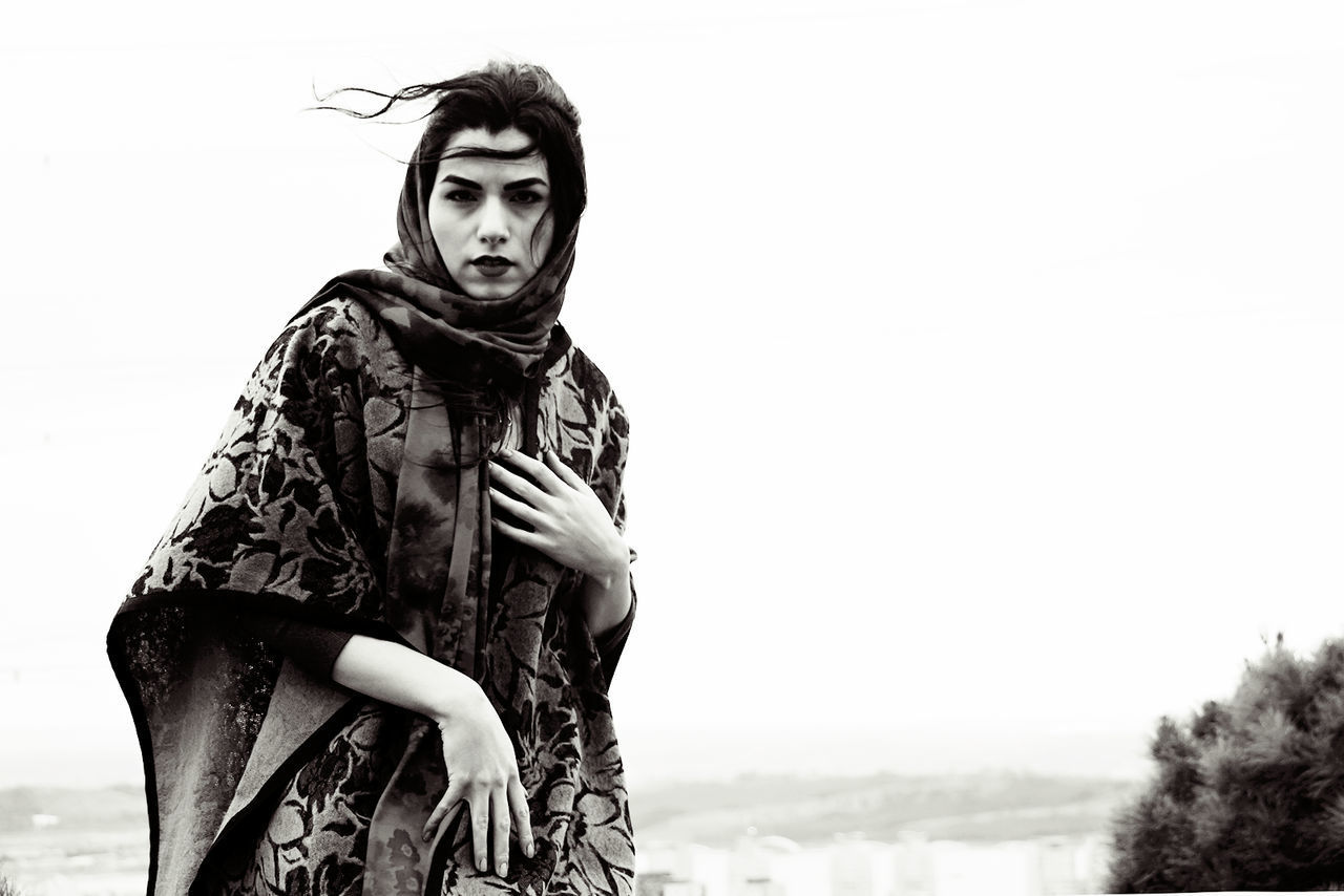 PORTRAIT OF YOUNG WOMAN STANDING AGAINST SKY