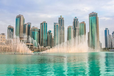 Modern cityscape by sea against sky