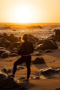 Rear view of man standing at beach against sky during sunset