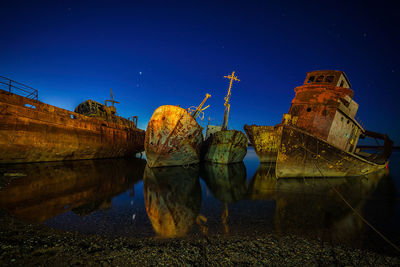 Reflection of abandoned boat in lake against clear blue sky at night