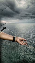 Close-up of hand sailing in sea against sky