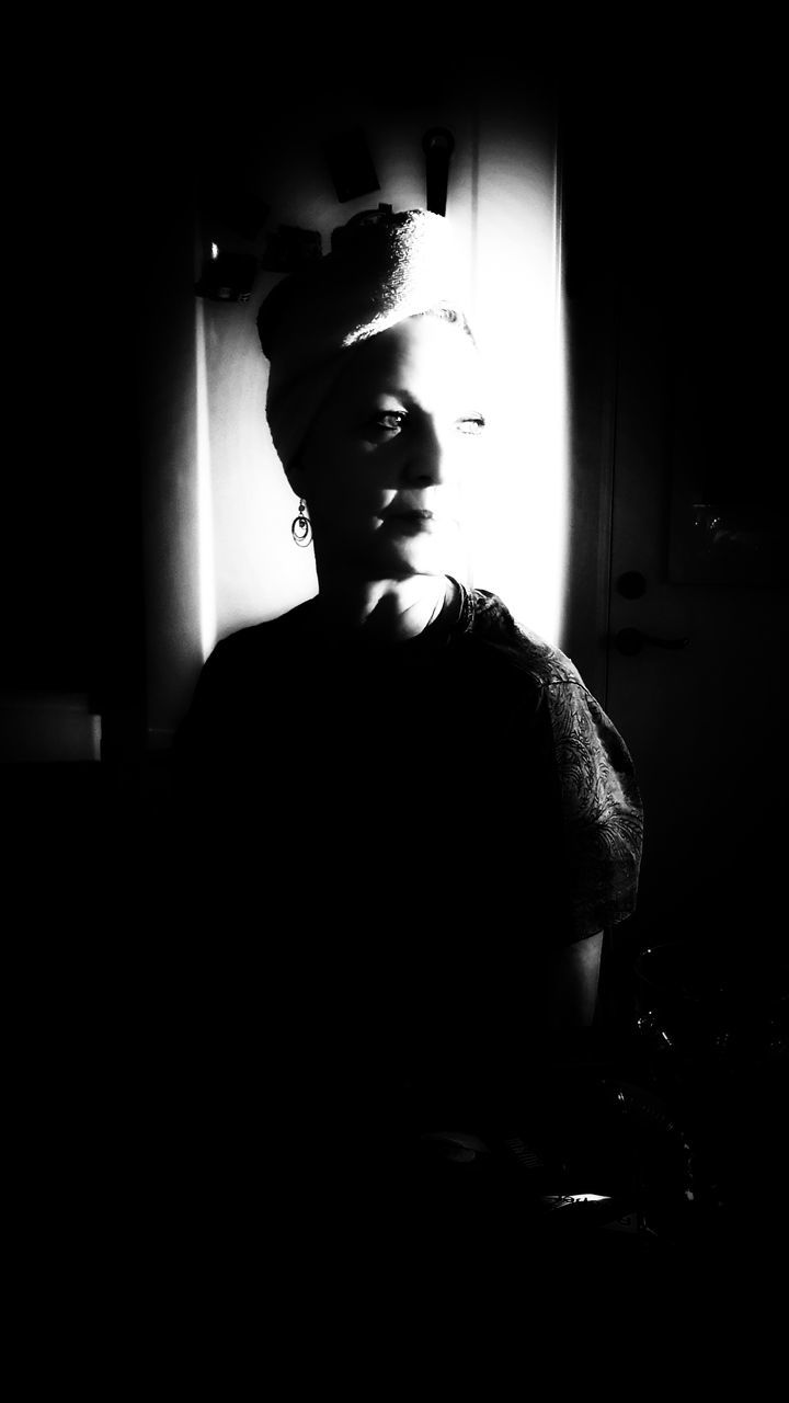 PORTRAIT OF YOUNG MAN LOOKING AWAY WHILE STANDING IN DARK ROOM