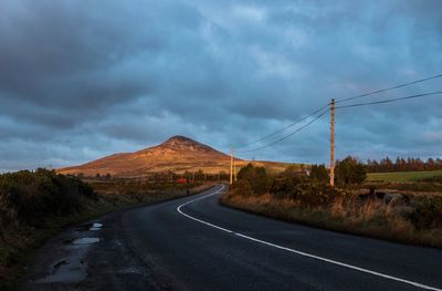 Road passing through landscape against dramatic sky