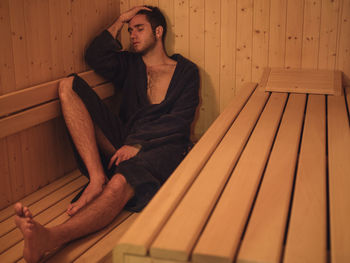 Young man wearing bathrobe relaxing in sauna