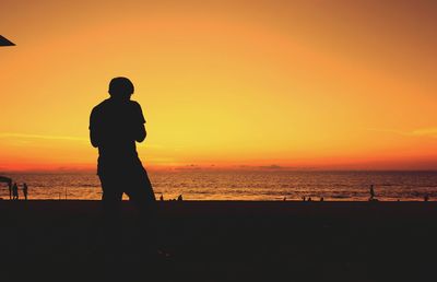Silhouette man standing at beach against orange sky