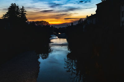 Silhouette trees by river against sky at sunset