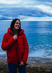 Portrait of young woman standing at beach against sky