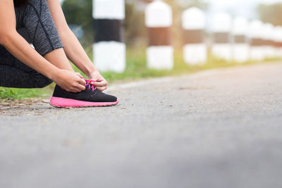 Low section of woman tying shoelace on road