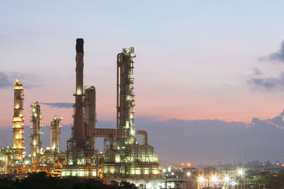 Illuminated factory against sky during sunset