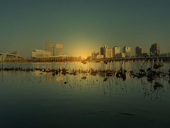 Scenic view of lake by buildings against sky during sunset