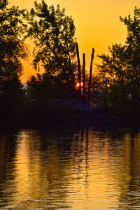 Silhouette trees by lake against sky during sunset