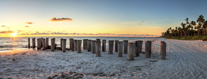 Wooden posts on beach against sky during sunset