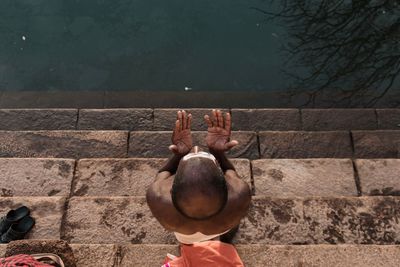 Directly above shot of shirtless man praying on steps at riverbank