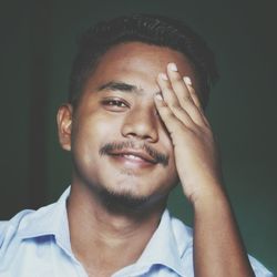 Close-up portrait of young man covering eye against wall